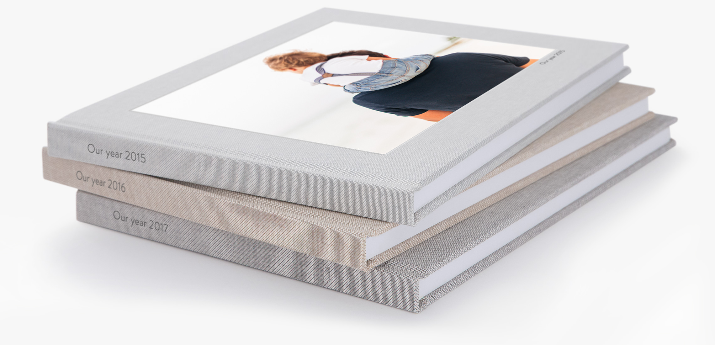 Pilha de três livros de fotografias quadrados com a fotografia de um rapaz aos ombros do pai na capa do livro no topo da pilha