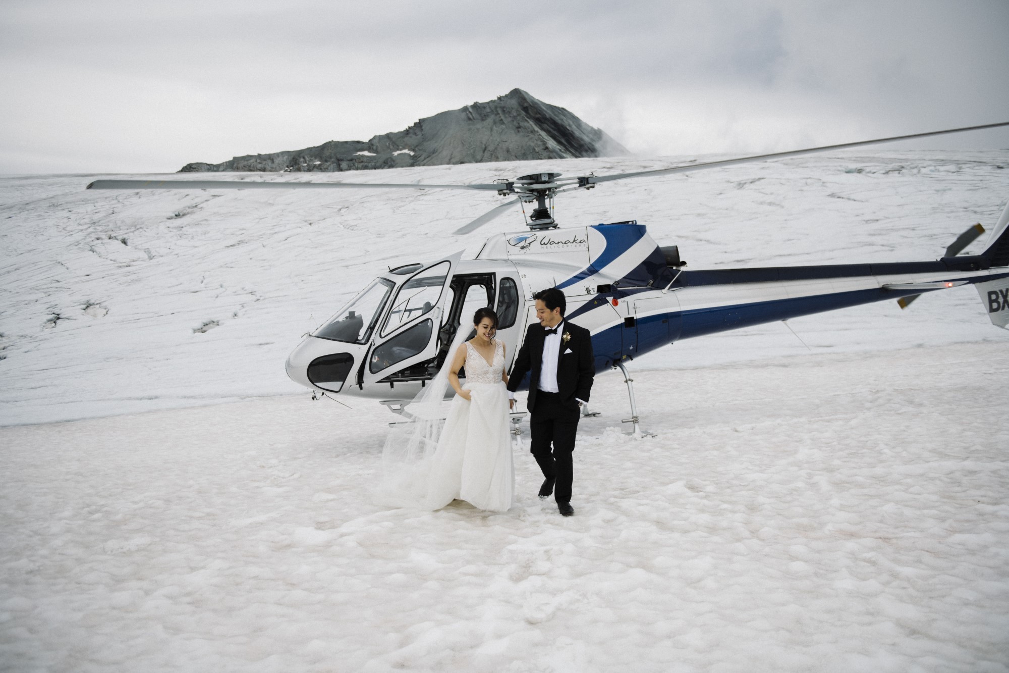 Bride and groom exit helicopter to snowy mountainside