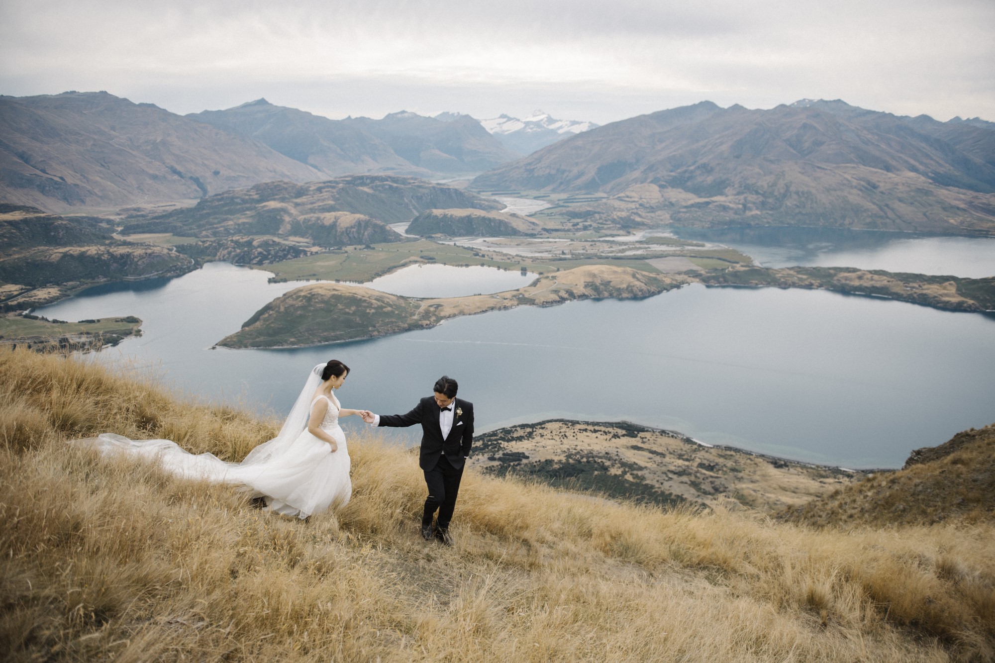 Bräutigam führt Braut den Hang eines Berges hinunter.