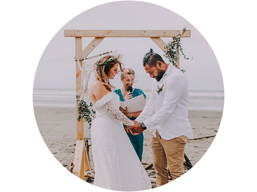 Bride and groom stand at beach altar while officiant conducts ceremony