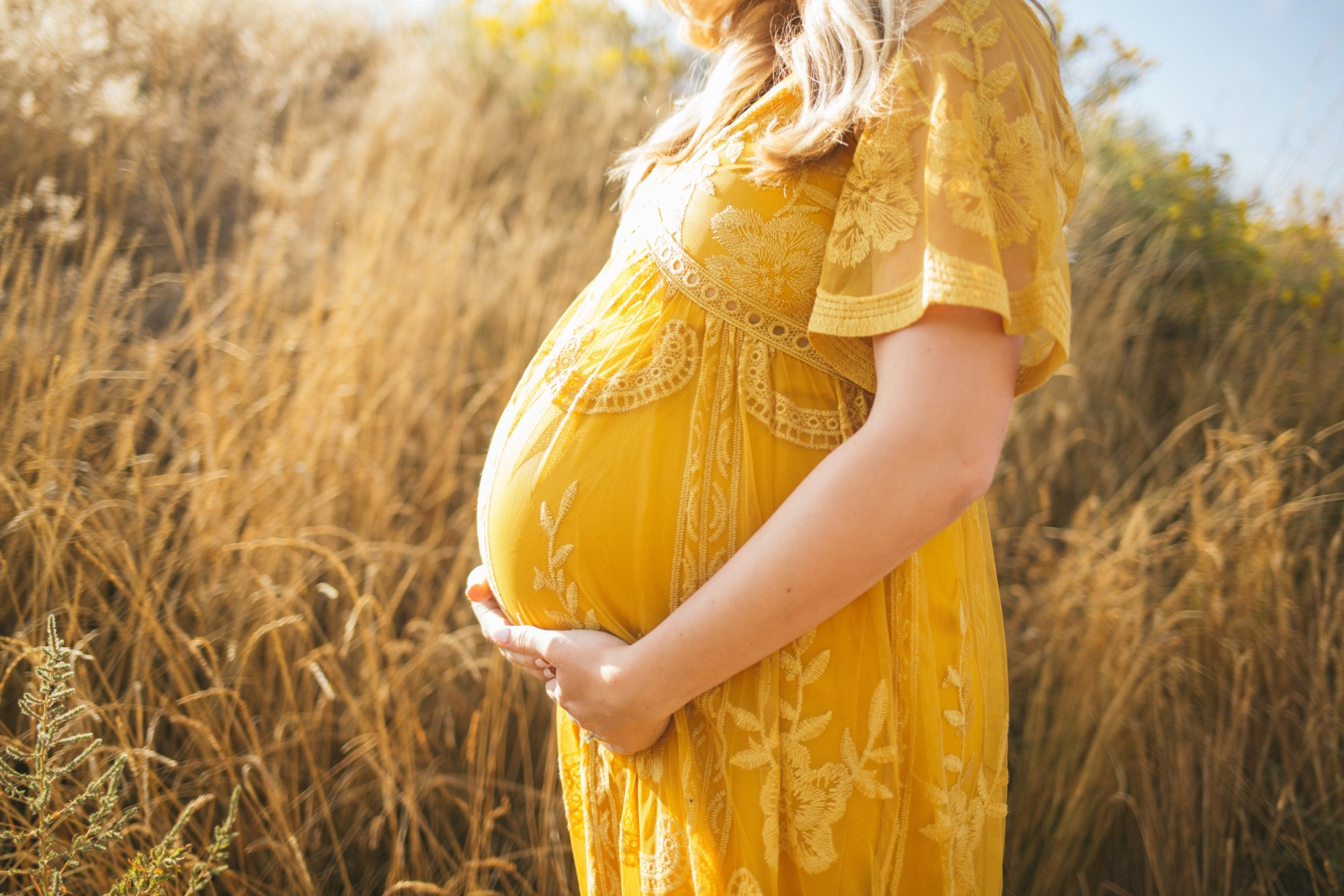 Woman in yellow dress in field holding her baby bump