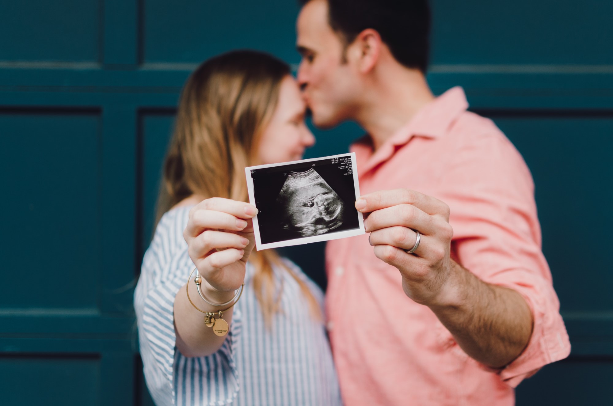 Ultrasound picture of baby being held by couple kissing in background