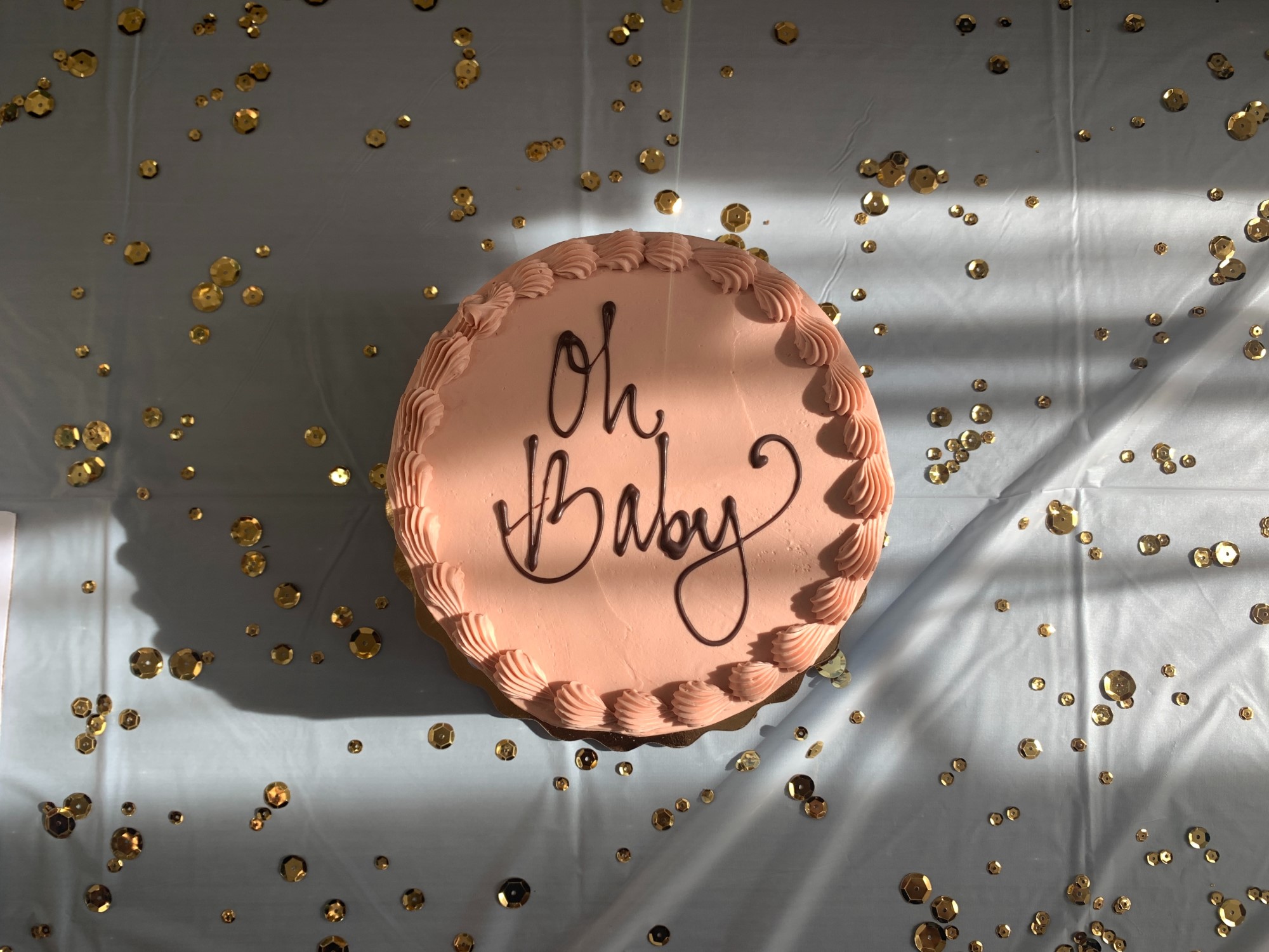 Pink cake on white tablecloth with icing spelling 'Oh Baby'