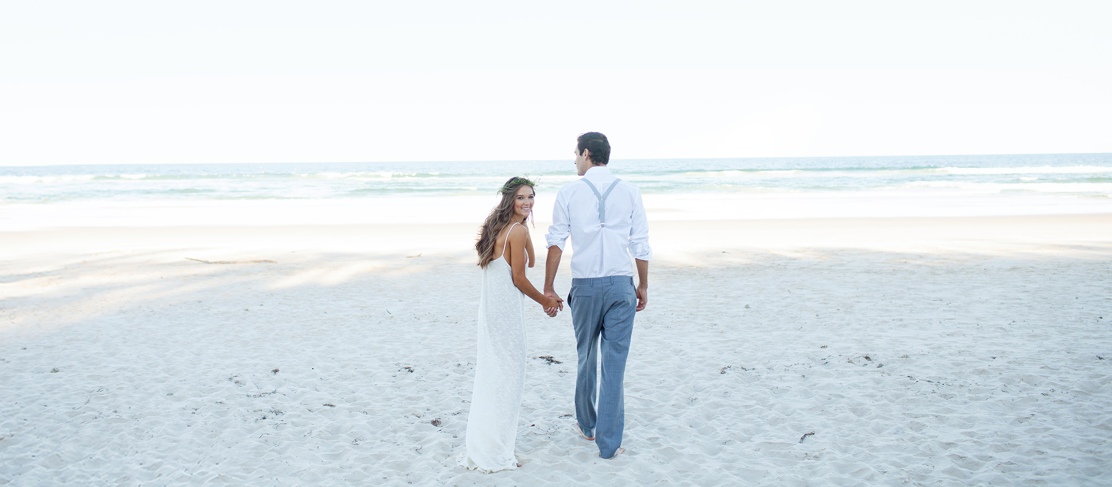 Newlyweds walking on white sand beach.