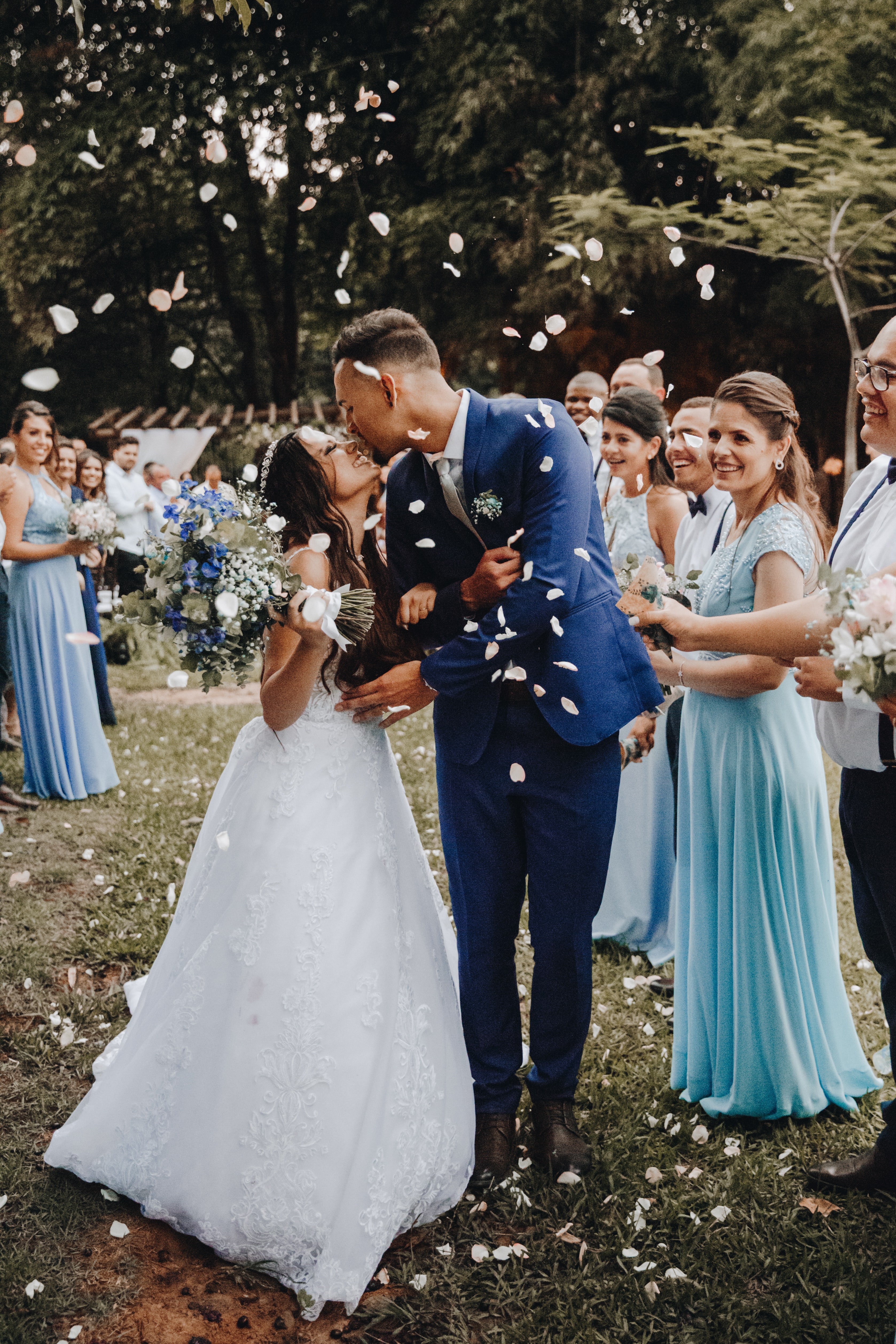 La mariée et le marié s'embrassent et sont aspergés de pétales de rose par la fête de mariage.
