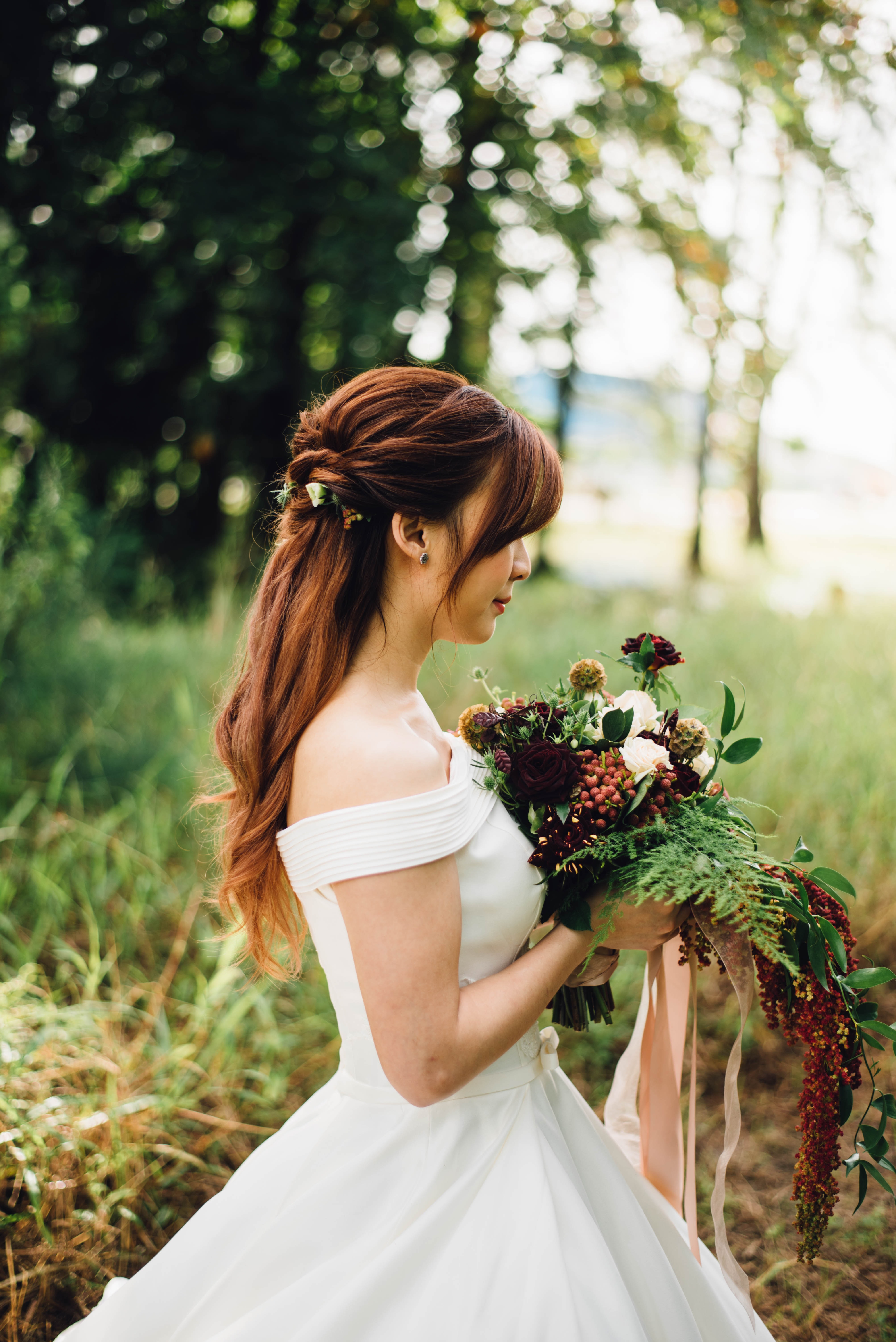 Portrait d'une mariée en robe blanche regardant son beau bouquet dans la forêt.
