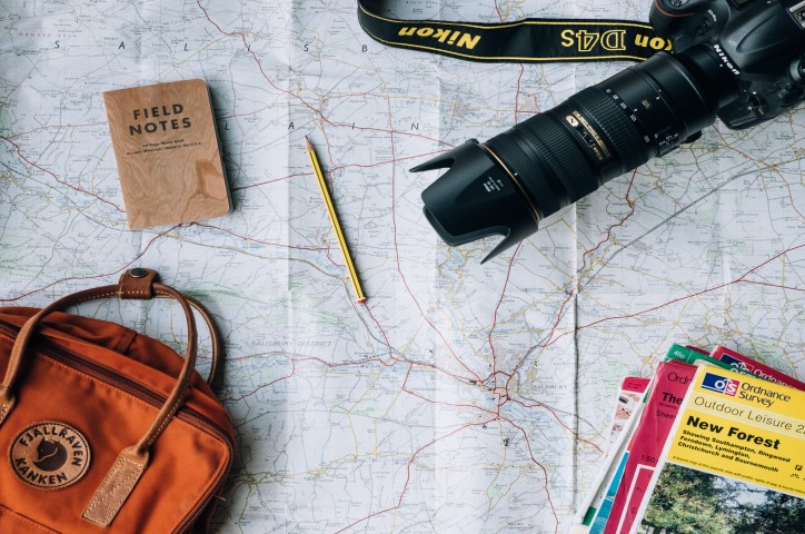 Carte ouverte avec un crayon, un sac de voyage et d'autres guides de voyage étalés dessus.