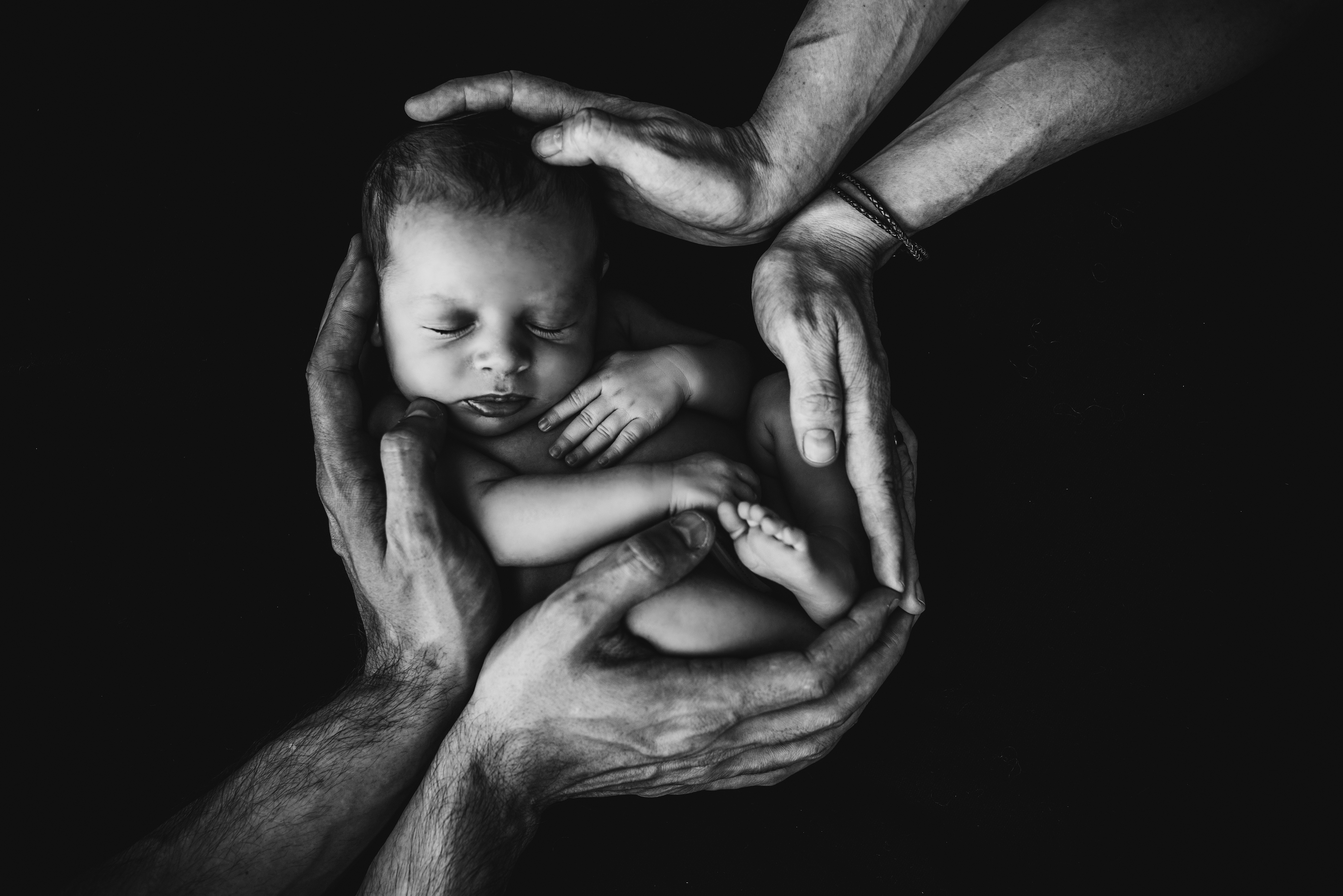 Image en noir et blanc d'un nouveau-né embrassé par ses parents.