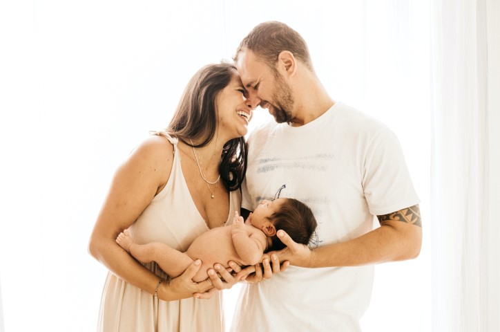 Eltern halten zusammen Baby in den Umarmen und lächeln.