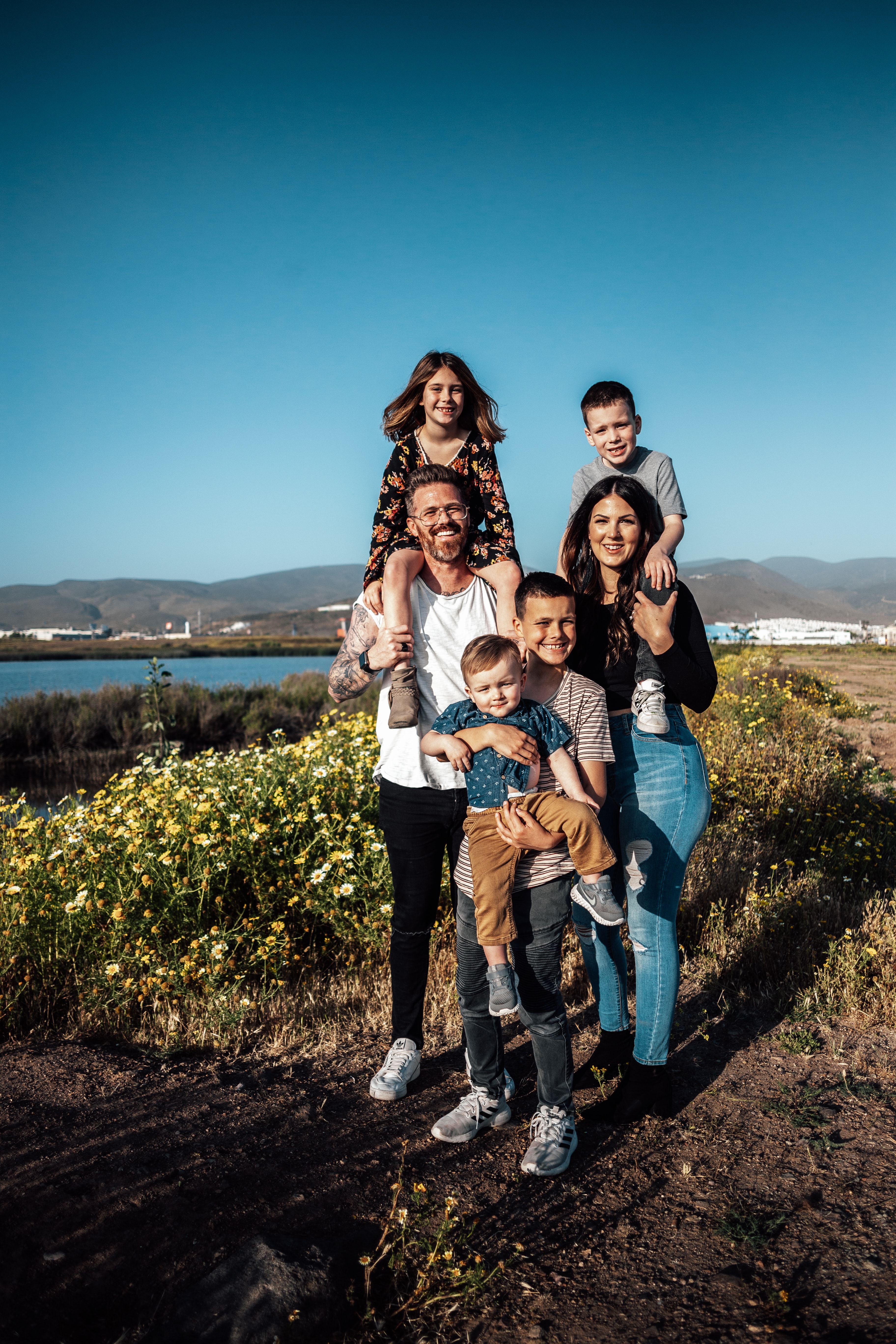 Familie steht in Natur-Umgebung und lächelt in die Kamera.