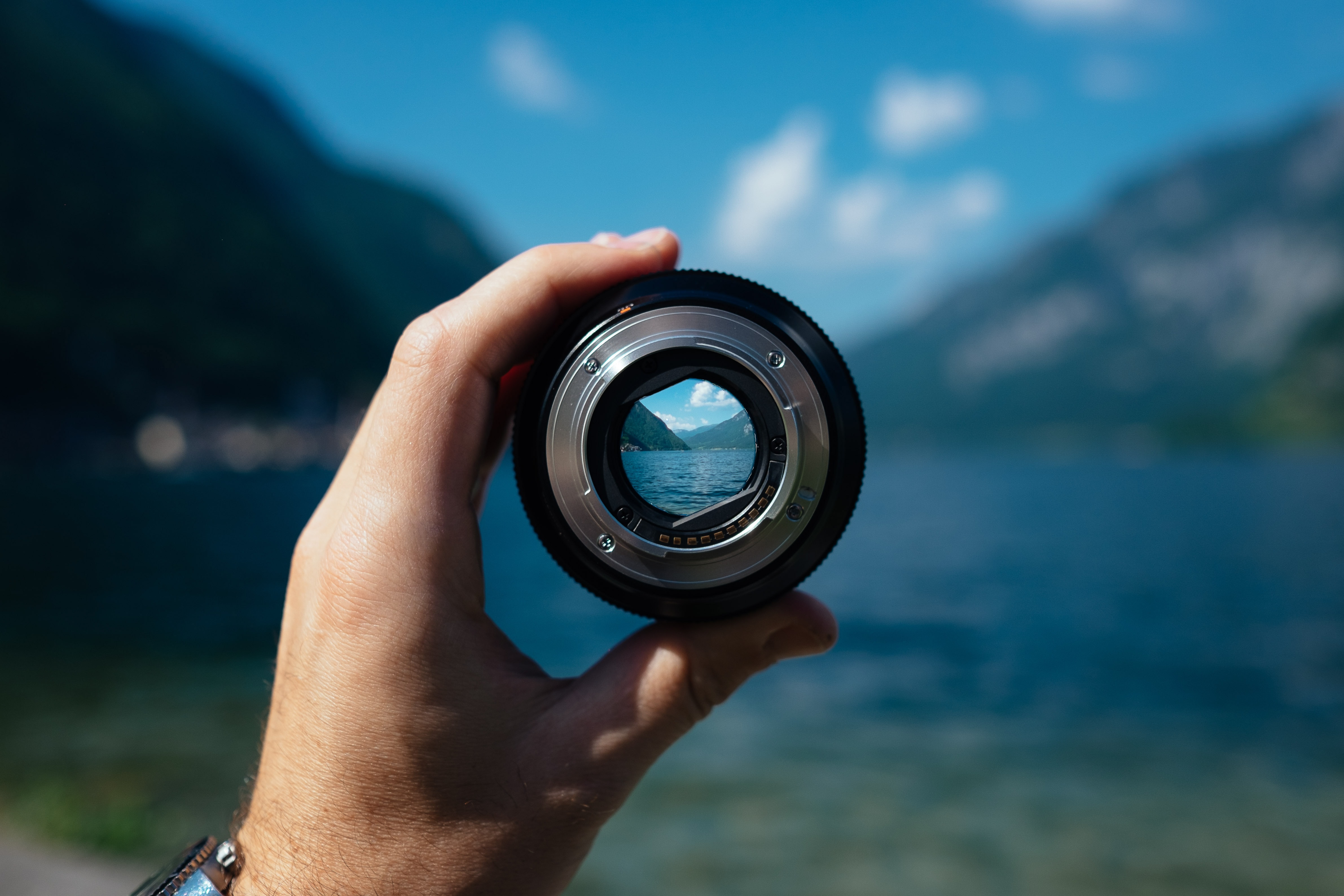 La main tient un objectif unique entouré d'un paysage lacustre.