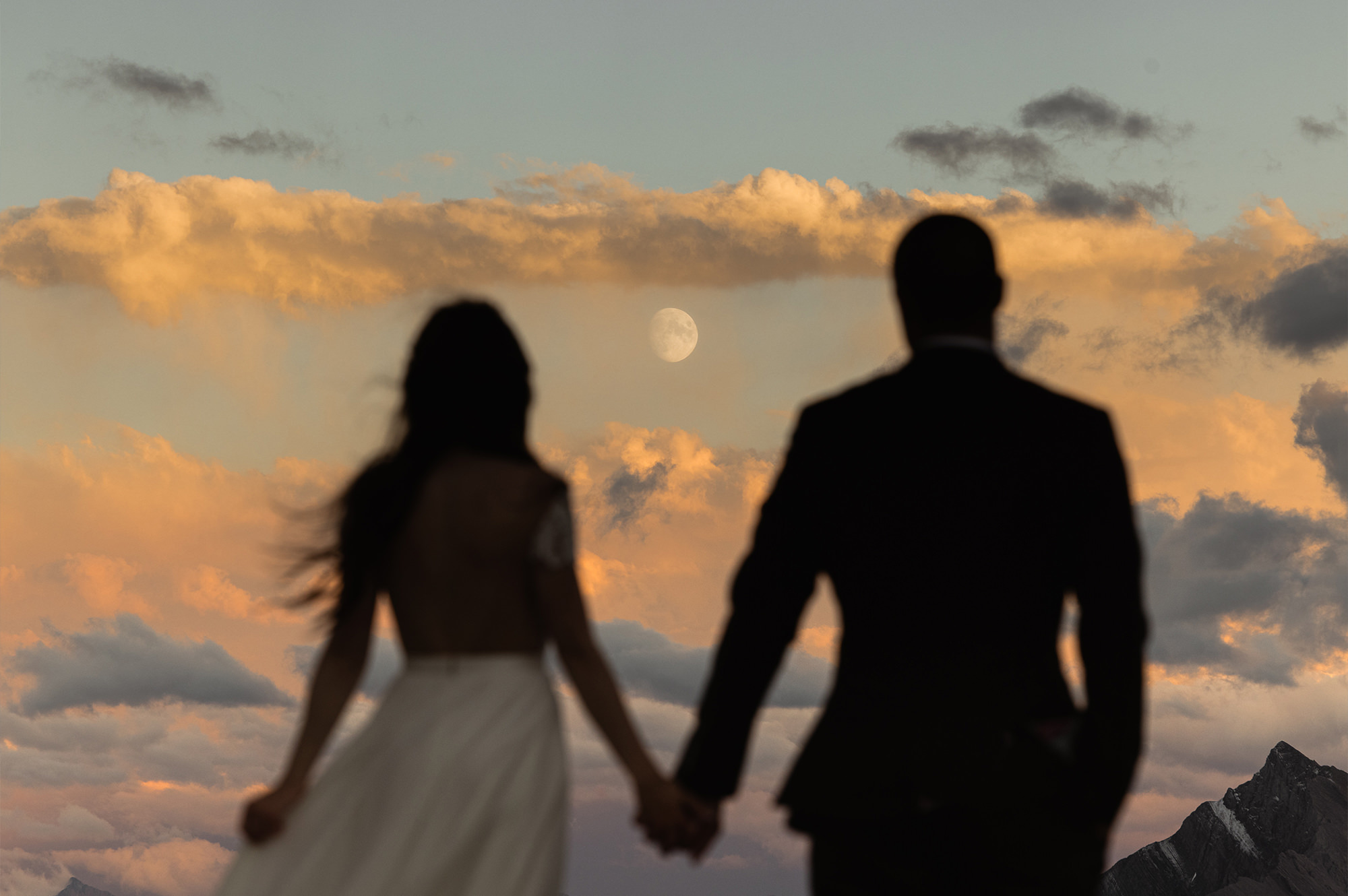 Braut und Bräutigam halten sich bei Sonnenuntergang an den Händen.