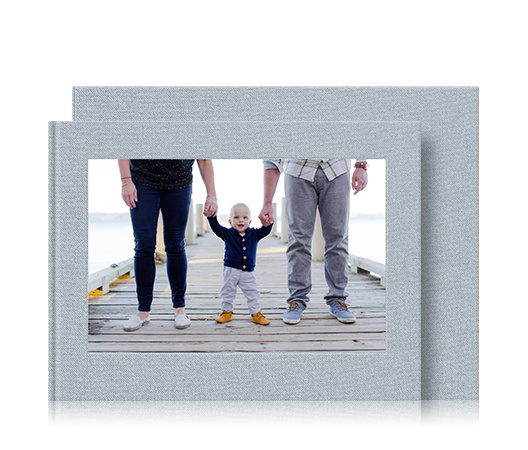 Livre photo de bébé au format paysage et boîte de présentation avec la photo de couverture d'un bébé tenant les mains de ses parents.