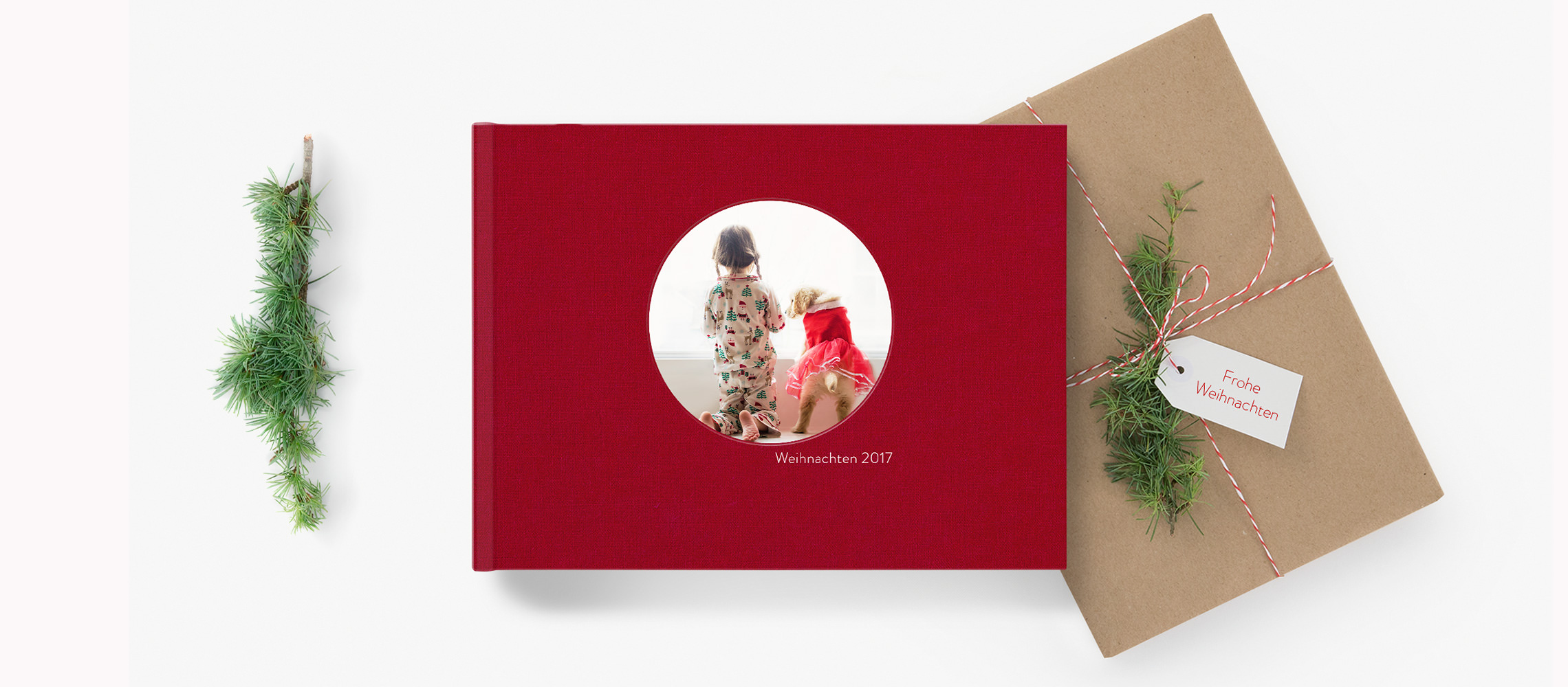 Ein rotes Fotobuch neben einem Weihnachtsgeschenk umgeben von Weihnachtsdekoration.