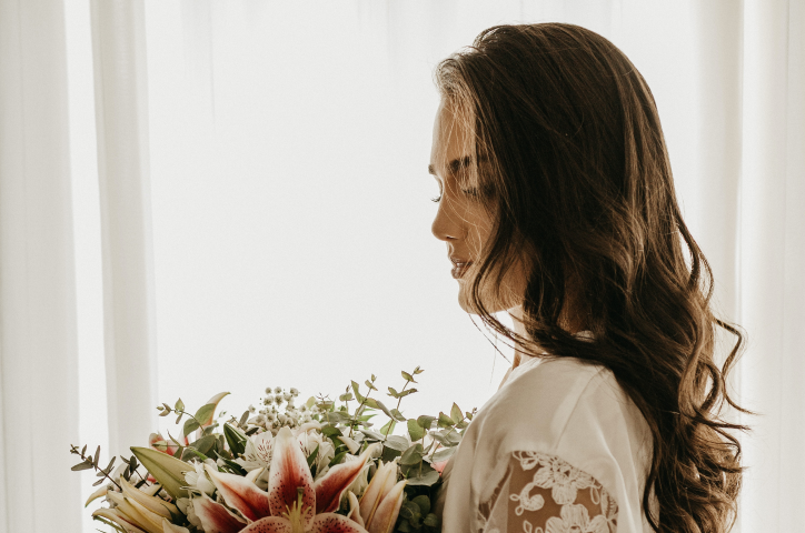 Braut in weißem Kleid hält kunstvollen Blumenstrauß in der Hand.