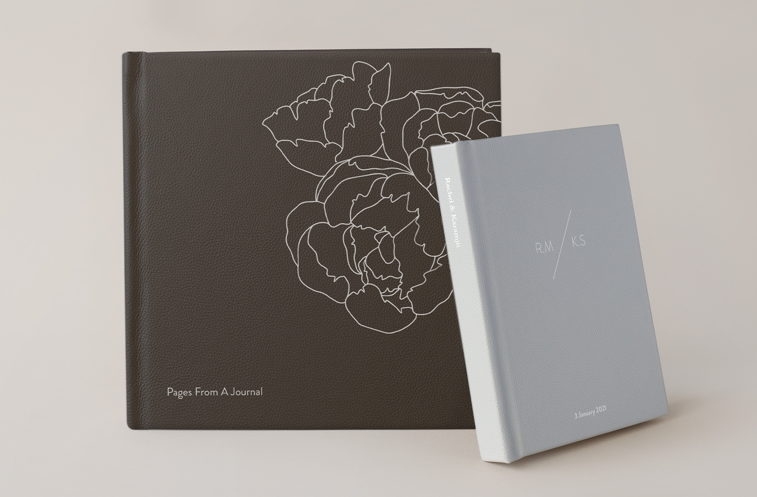 Álbum de fotos de cuero mocca con cubierta de diseño plateado junto a un álbum de cuero gris plateado.