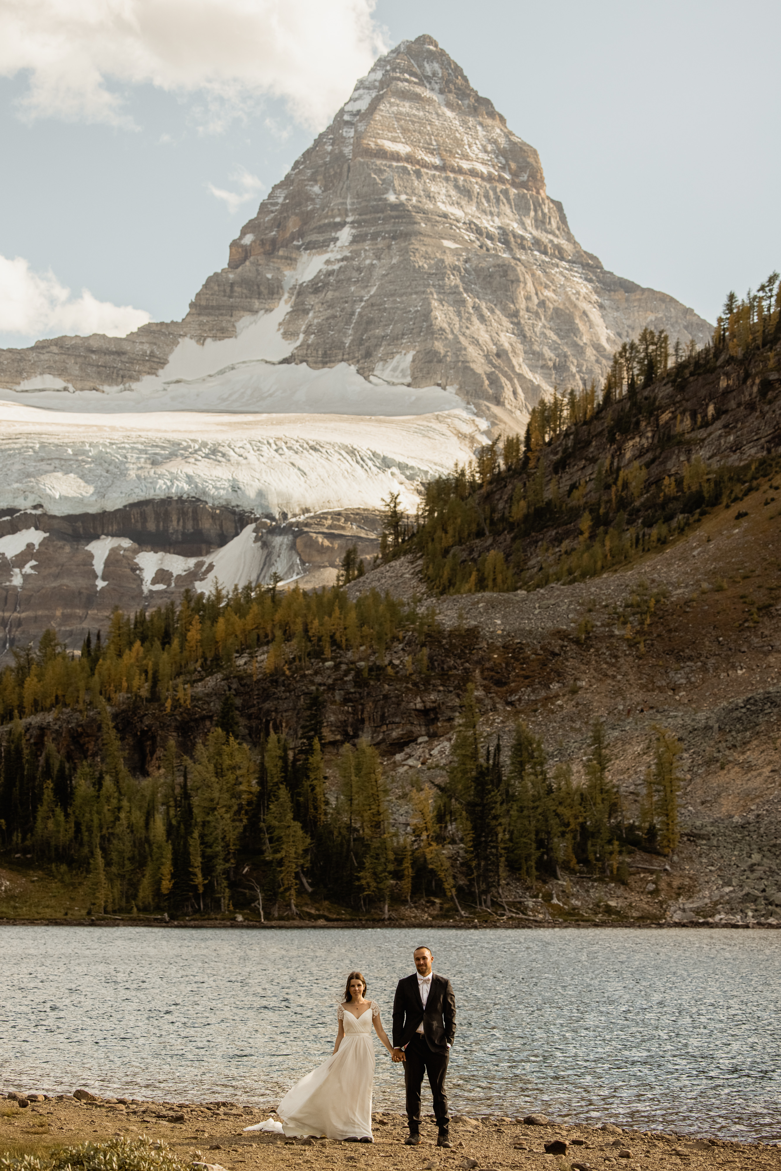 Drone shot of newlywed couple posing for portrait under mountains.