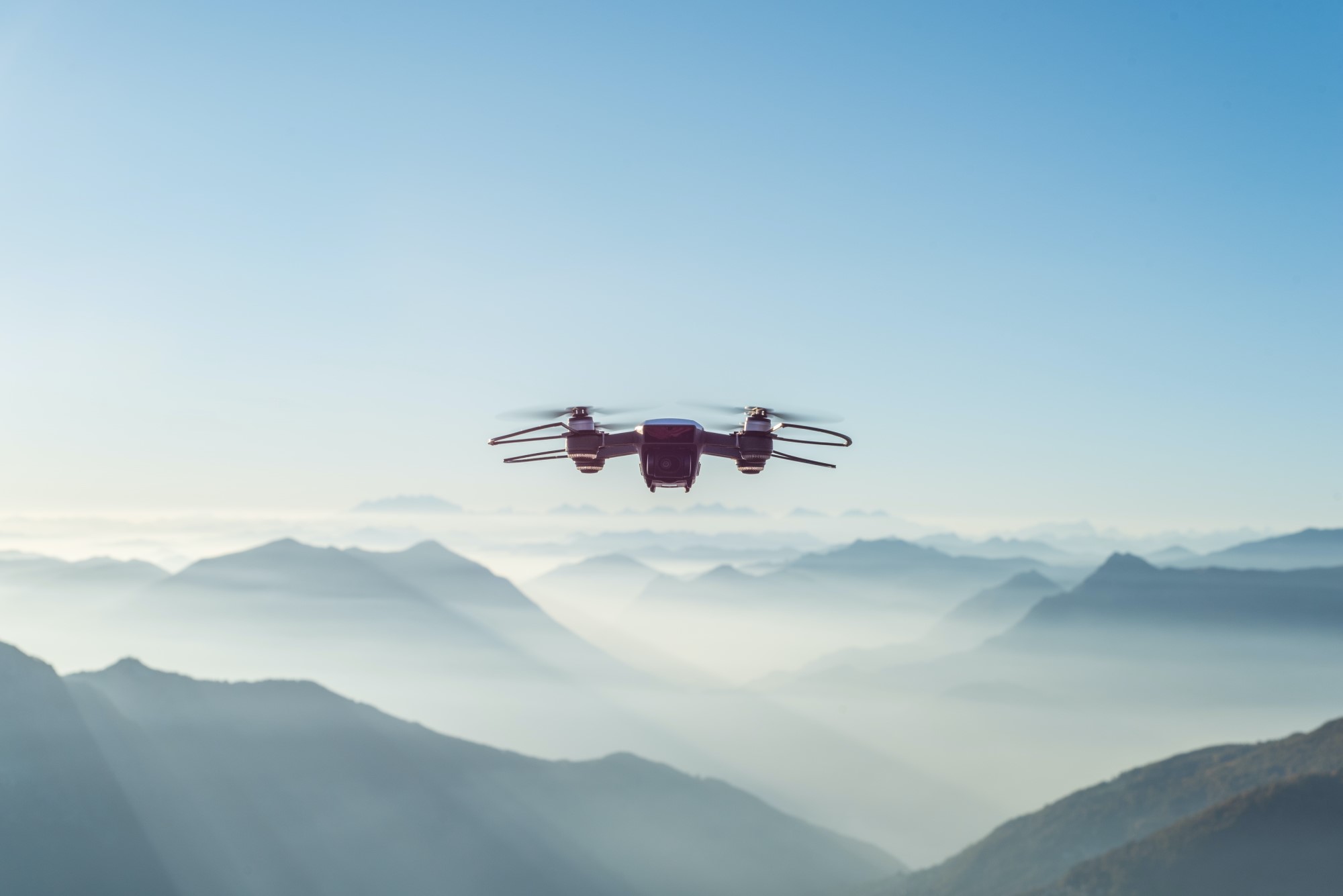Image of drone floating above mountains in daylight.