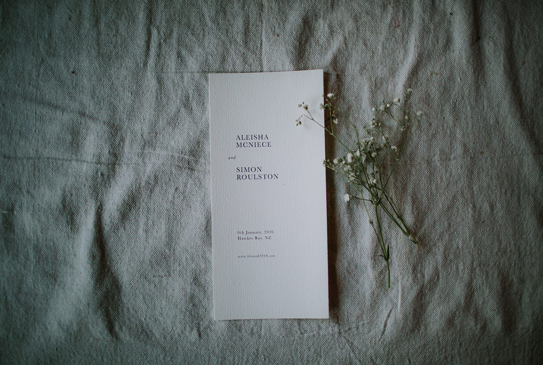 Minimal wedding invitation and delicate flowers set on top of grey linen fabric