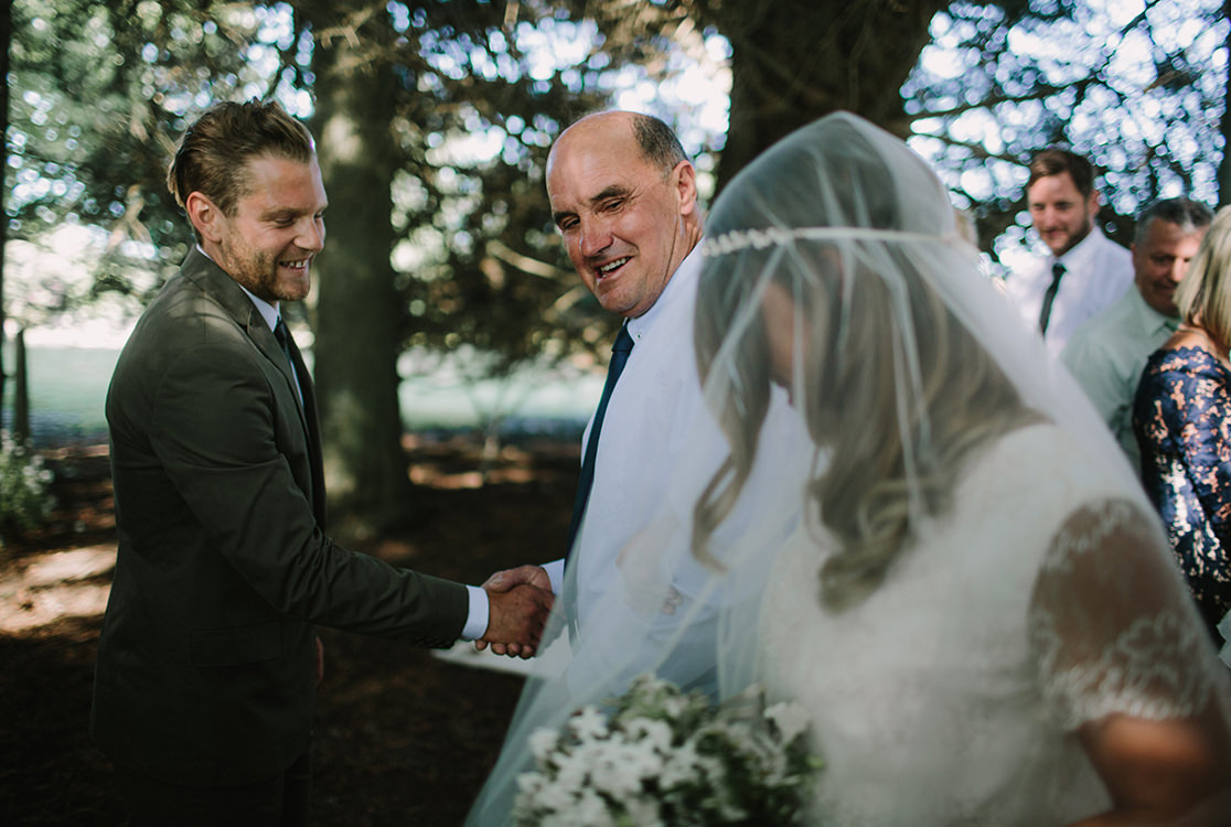 Le marié et le beau-père se serrent la main et regardent la mariée.
