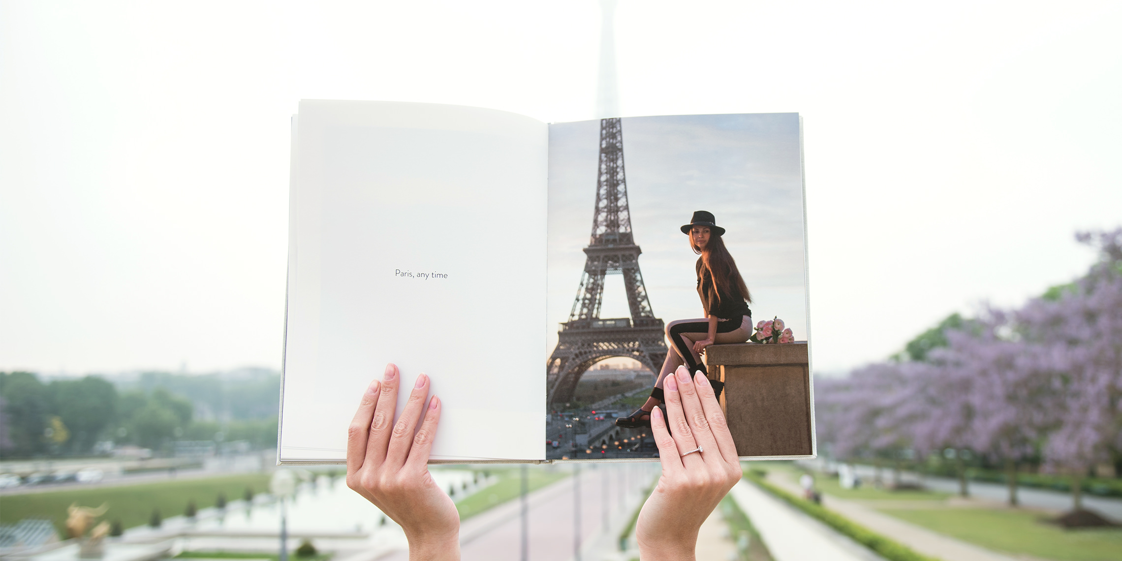 Hands holding portrait photo book in front of the Eiffel Tower.