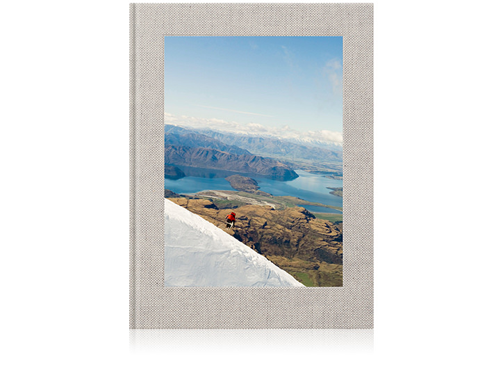 Hochwertiges Leinen-Reise-Fotobuch mit Berg- und Seelandschaft auf dem Cover.