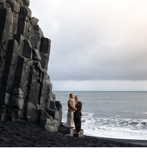 Bride and groom pose on black sand shore