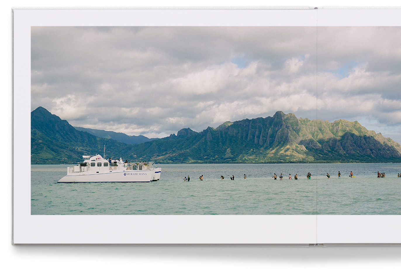 Premium-Fotoalbum aus Leder mit einem Bild von einem Boot und Menschen im Meer und Berglandschaft im Hintergrund.