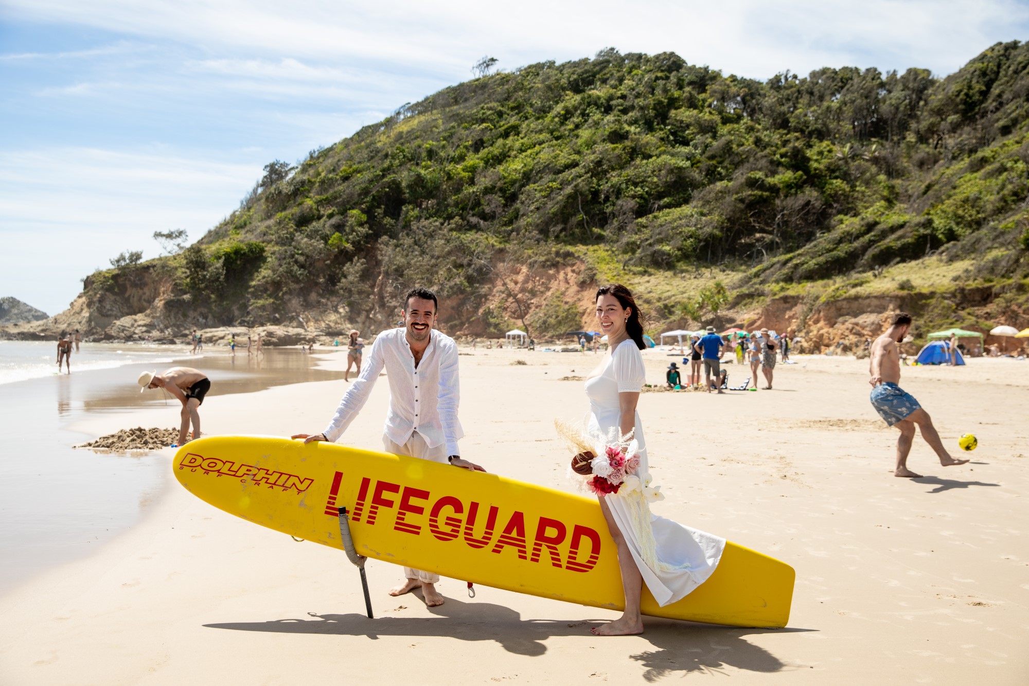 Wedding couple on beach with lifeguard surfboard