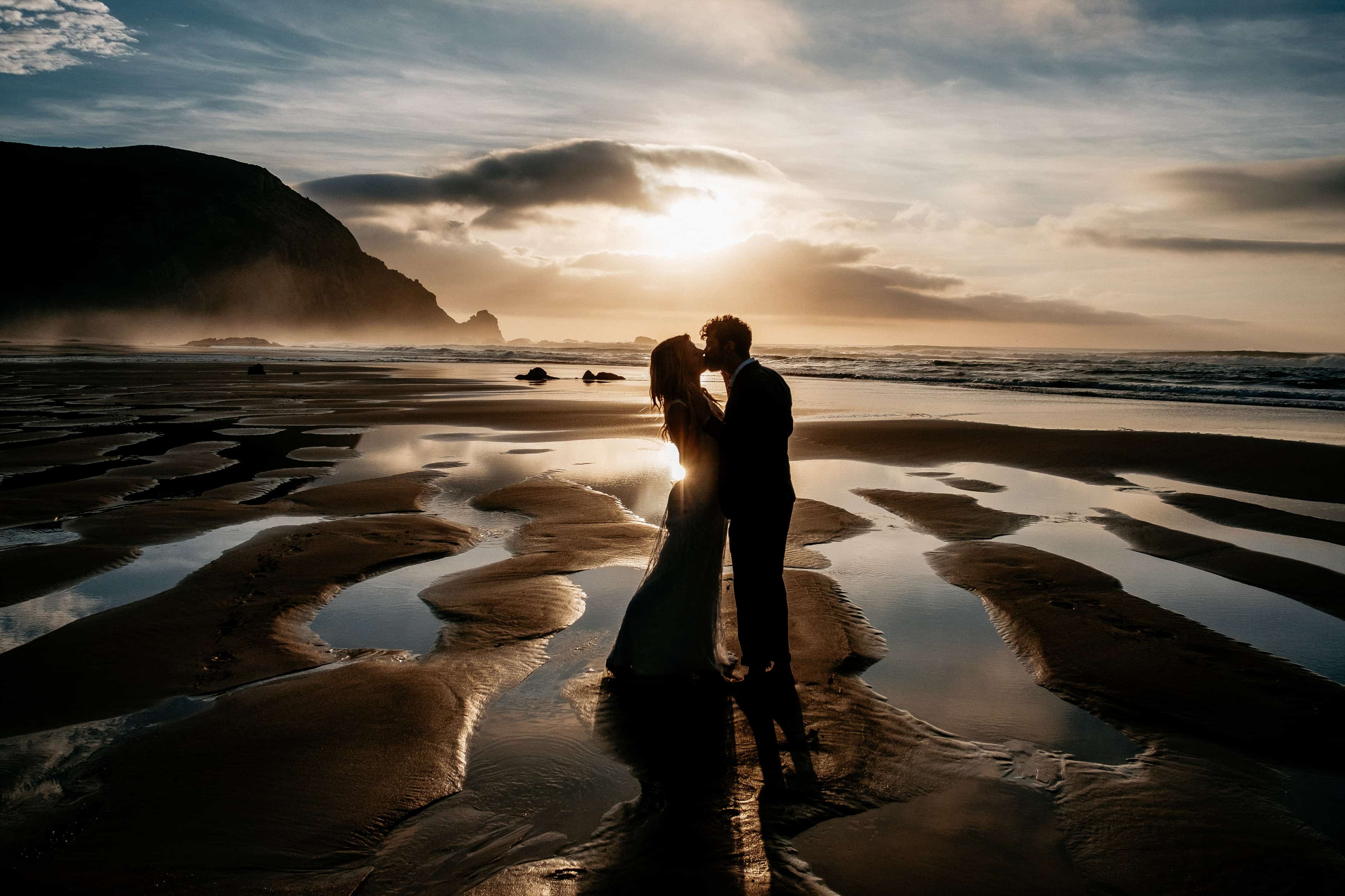 Brautpaar küsst sich am Meer bei Sonnenuntergang.