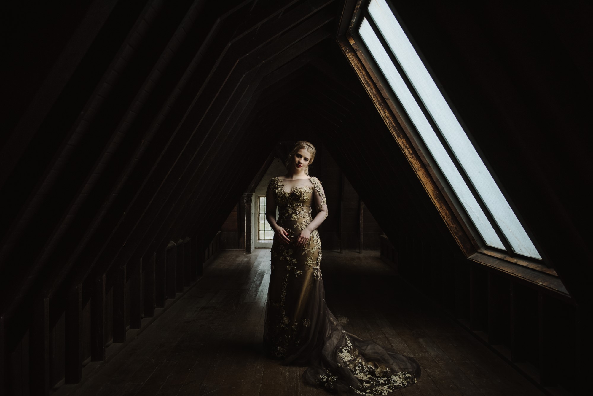 Bride in dark wooden hallway of an attic wearing a dark gold floral wedding dress with a train