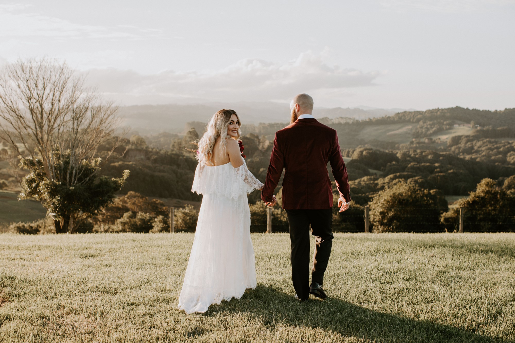 Bride and groom couple walking on field, the bride facing towards the camera wearing lace wedding dress