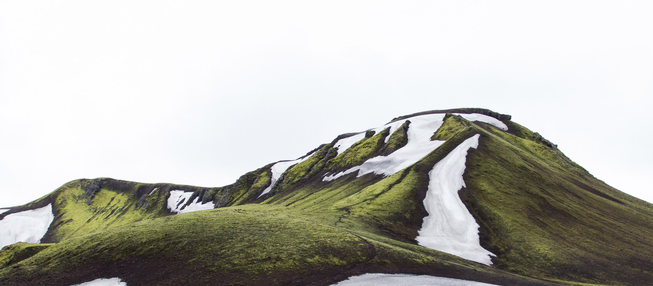 Landscape photo of green mountains with snow and ice patches.