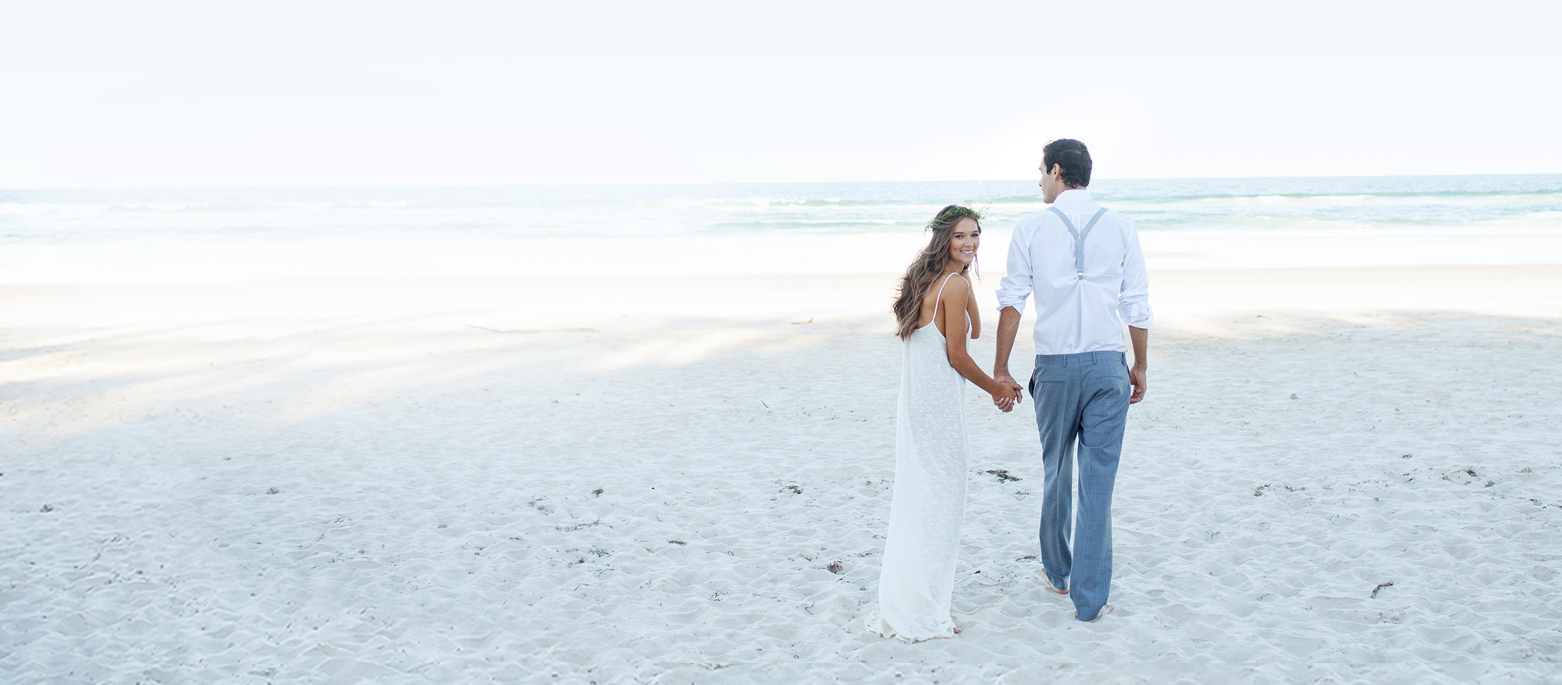 Couple holding hands at the beach on their wedding day.