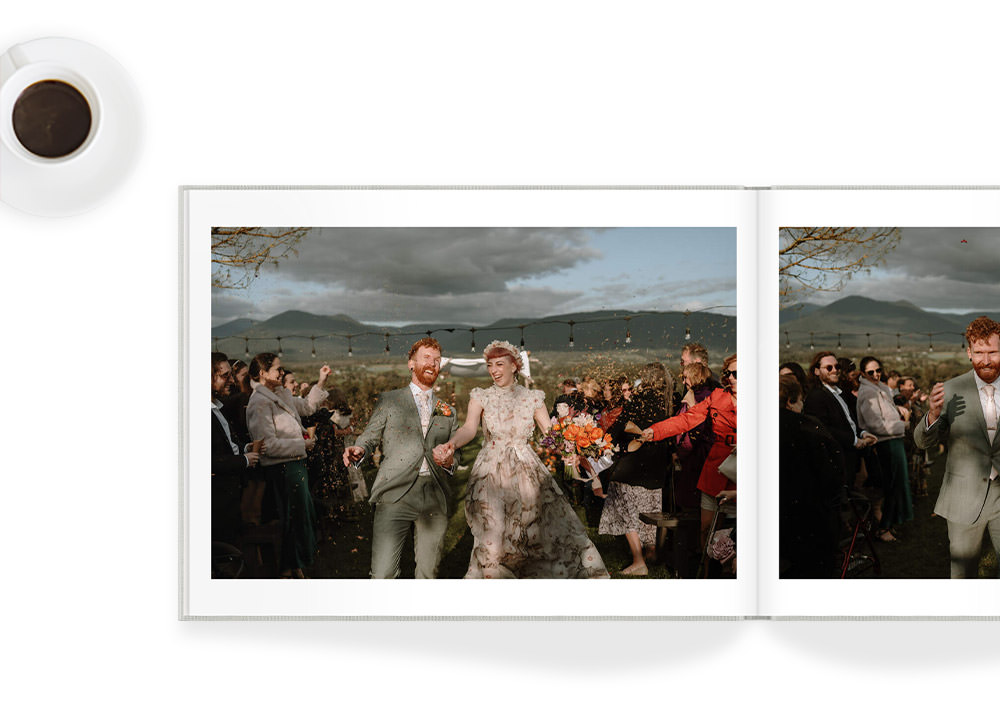Open landscape photo book with wedding couple inside - book in on white background with cup of coffee beside it