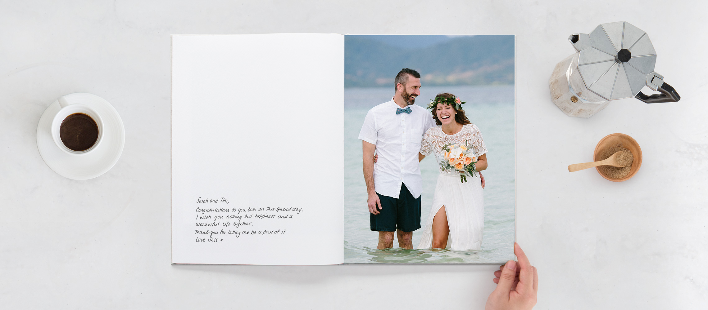 Livre d'or ouvert avec des mariés souriants dans l'eau et une inscription sur la page blanche.