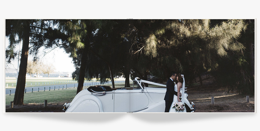 Wedding portrait of newlywed couple alongside a classic white car.