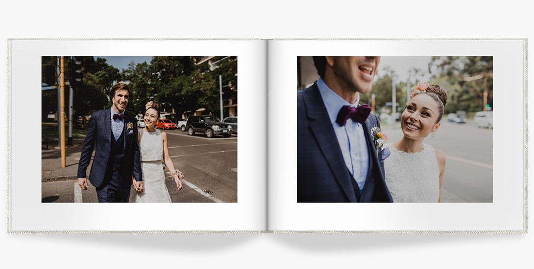 Landscape wedding album laying open with two photos of newlyed couple in wedding dress and suit walking across the street