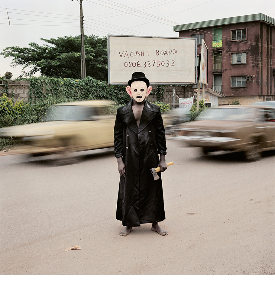 Masked man holding small axe in street - Escort Kama, Enugu, Nigeria, 2008.