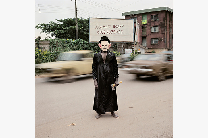 Masked man holding small axe in street - Escort Kama, Enugu, Nigeria, 2008.
