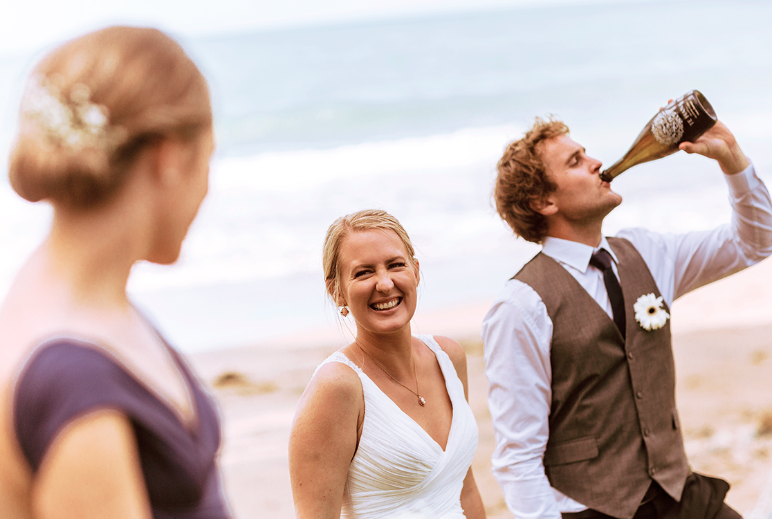 Bride and groom at the beach. Groom drinking from a champagne bottle