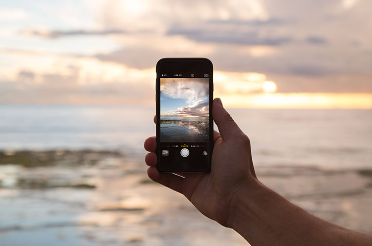 Appareil photo iPhone tenu à la main prenant une photo d'un coucher de soleil à la plage.