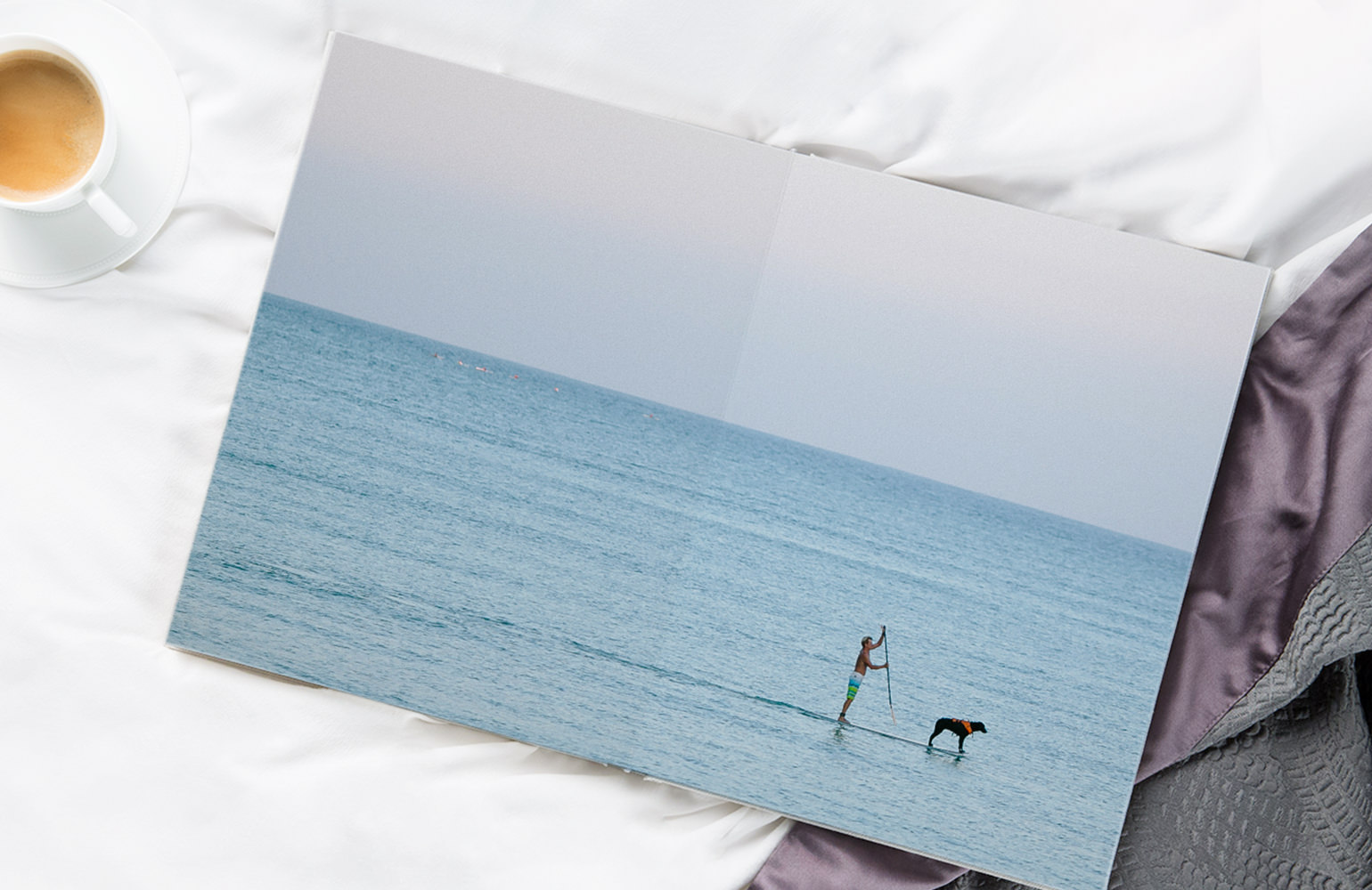 Portrait photo album laying on bed open to a double page spread of man paddle boarding with dog