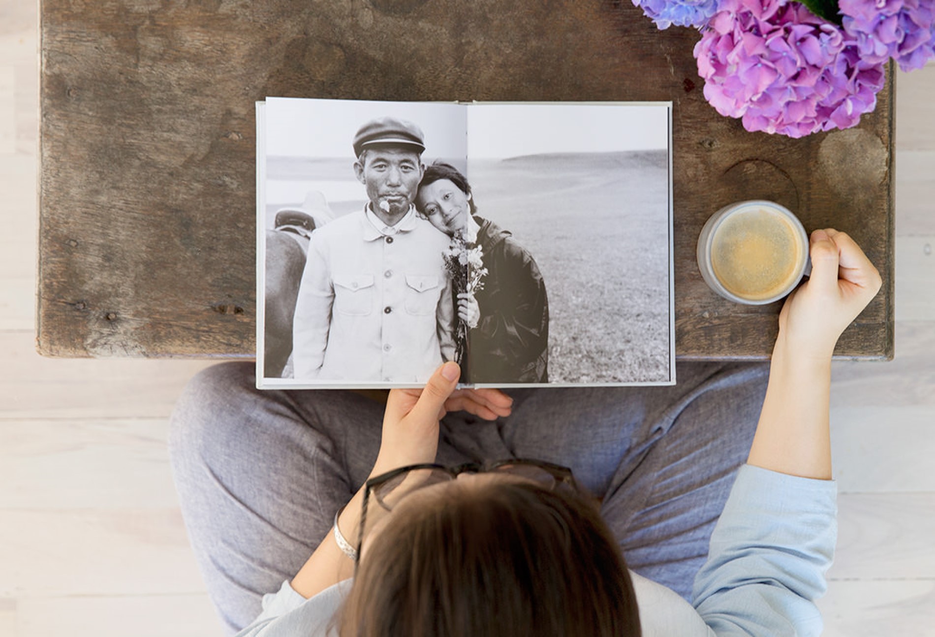 Woman viewing open photo book at coffee table with cup of coffee