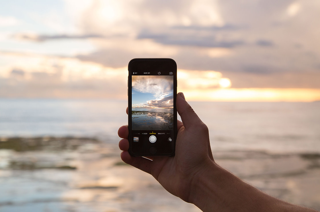 Hand holding phone taking a photo of the ocean