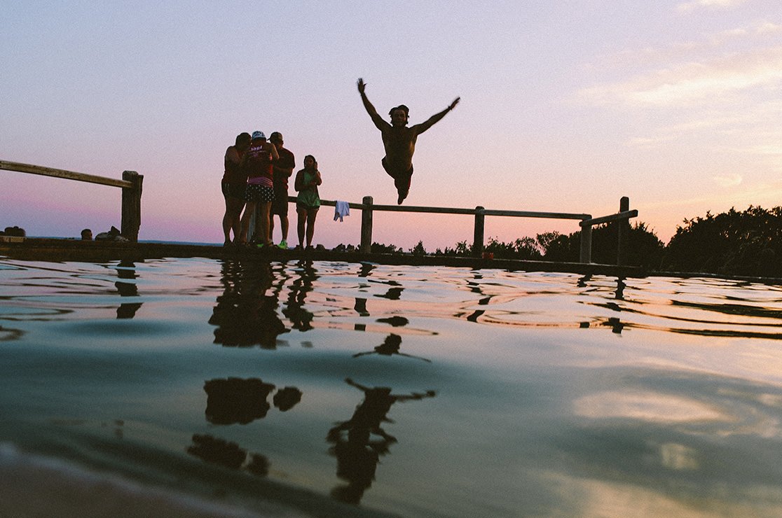 Friends jumping into a lake at sunset