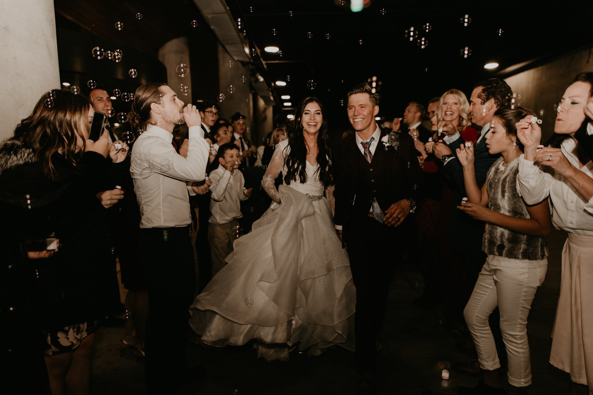 A newlywed couple surrounded by friends and family blowing bubbles.