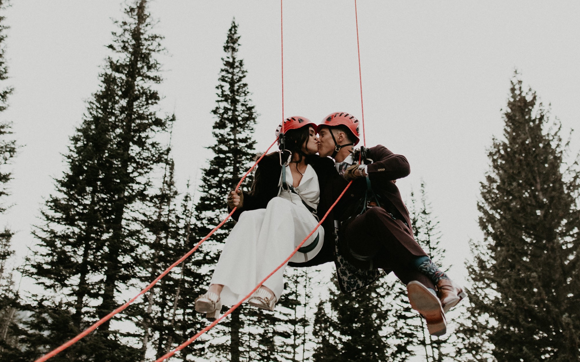 Newlywed couple kissing whilst hanging in harnesses.