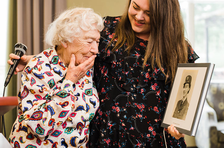 Older woman embraced by a younger woman, looking at an old portrait.