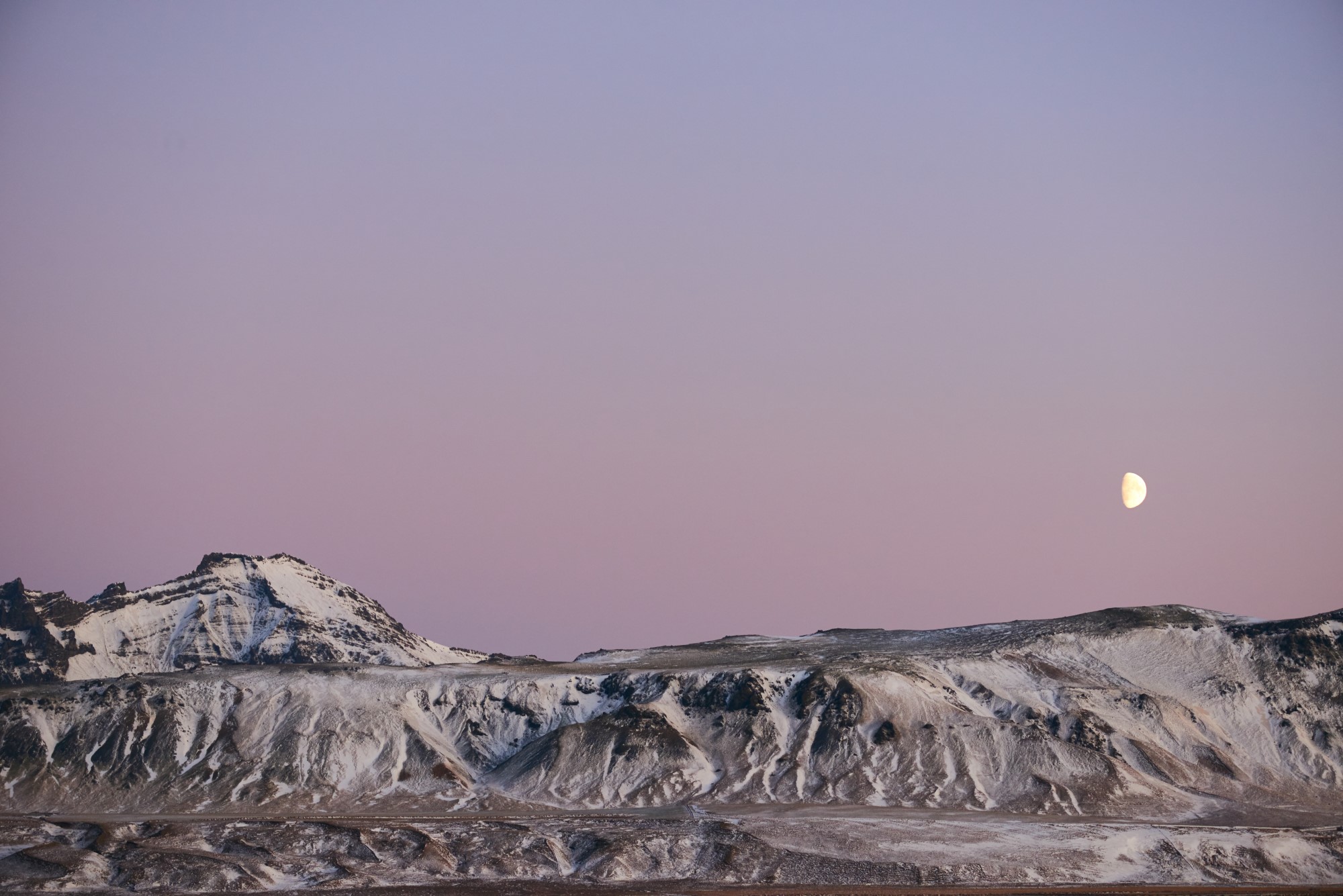 Snow-covered mountain with moon in sky.